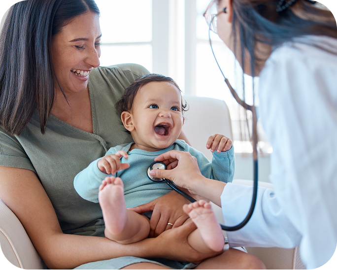 A pediatrician examines a laughing baby held by a parent