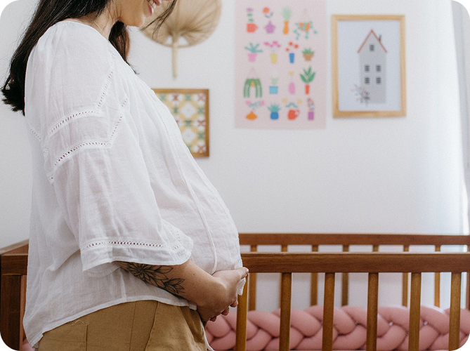 A pregnant woman standing beside a crib in a nursery
