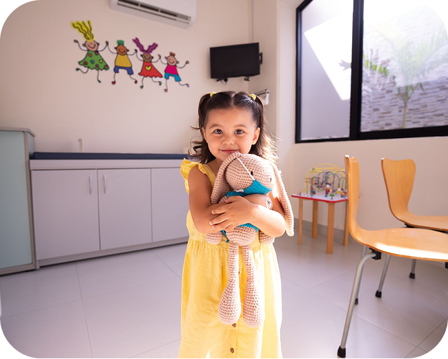 A young girl hugging a stuffed animal in a clinic exam room