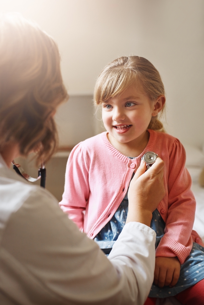 A doctor listens to a smiling young girl's chest with a stethoscope during an exam