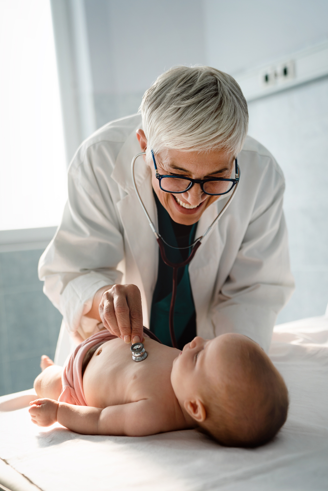 A smiling doctor listens to a newborn baby's chest with a stethoscope
