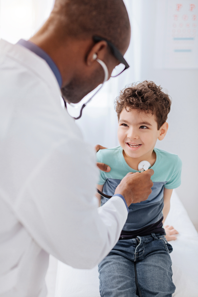 A pediatrician listening to a young boy's chest with a stethoscope
