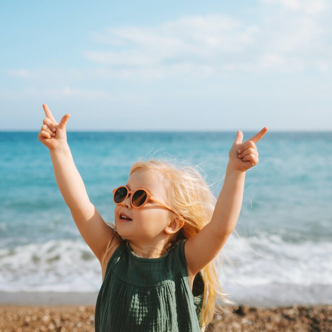 A young girl in sunglasses raising her arms on the beach
