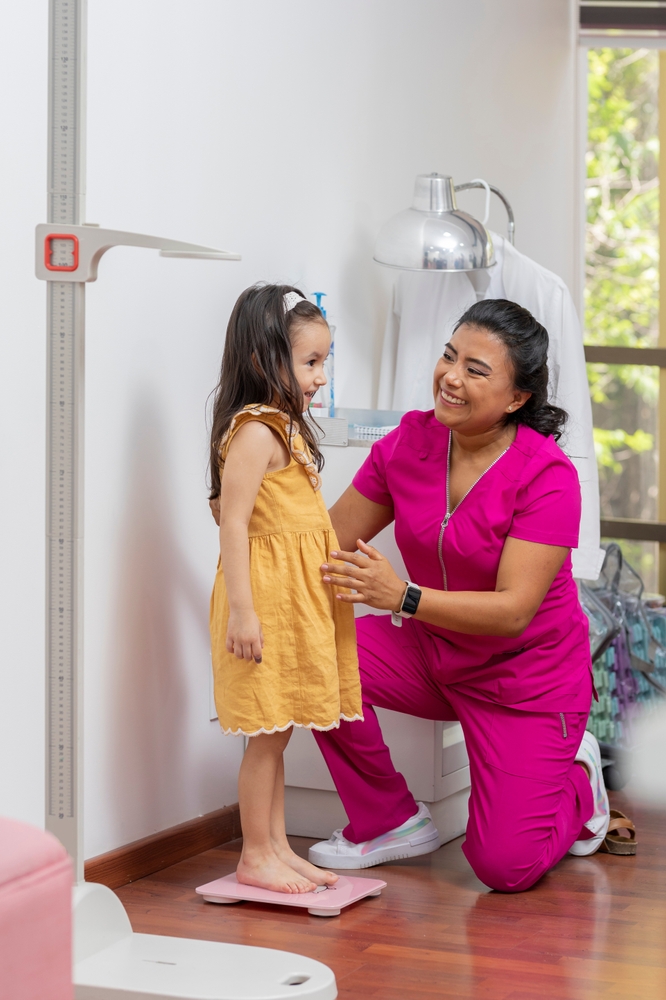 A provider helping a young girl step onto a height measurement scale