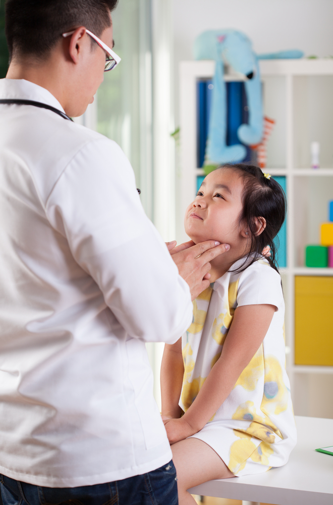A pediatrician gently examining a young girl's neck during a checkup