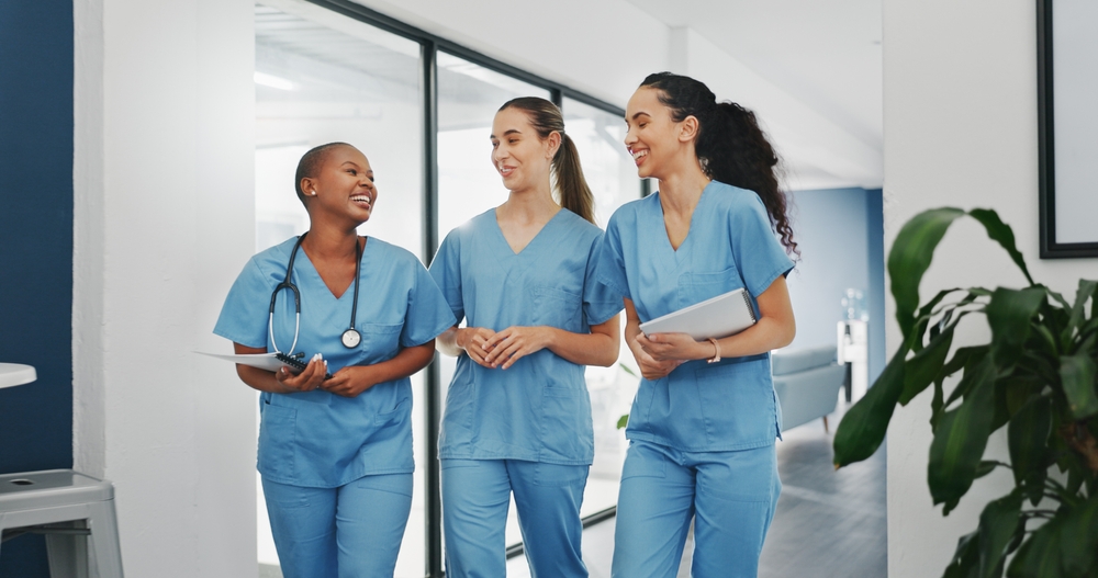 Three nurses in scrubs walking and talking together in a hallway