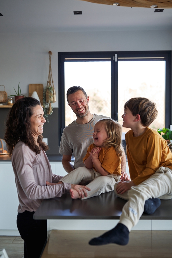 A family of four laughing together in their kitchen