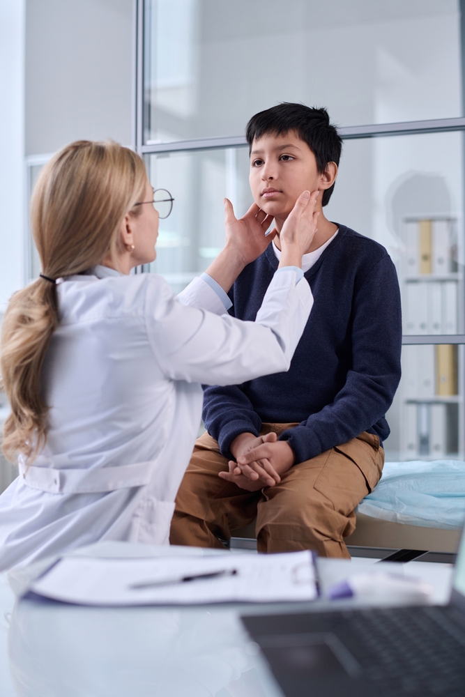A provider examining a teen boy's neck and throat during an exam