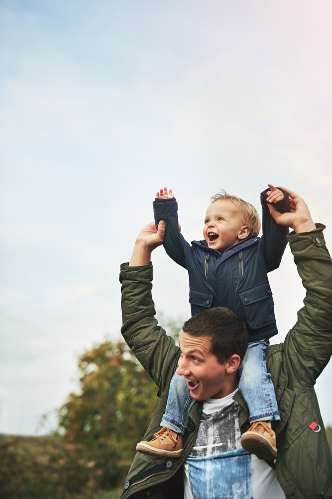 A father lifting his laughing toddler onto his shoulders outdoors