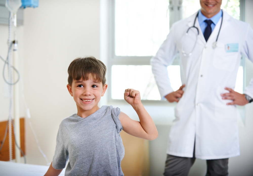 A young boy flexing his arm and smiling with a provider in the background