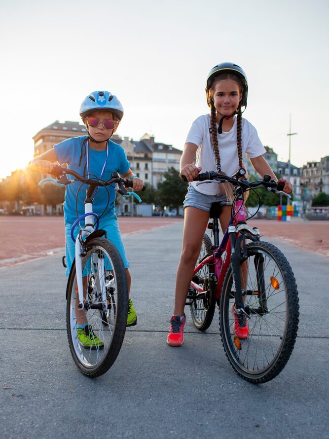 Two children wearing helmets and riding bikes outdoors