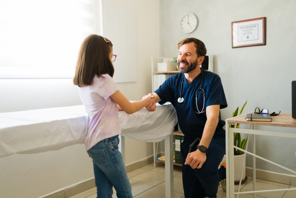 A pediatrician shaking hands with a young girl patient in an exam room
