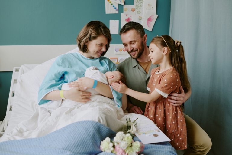A family of four smiling together around a newborn in a hospital room