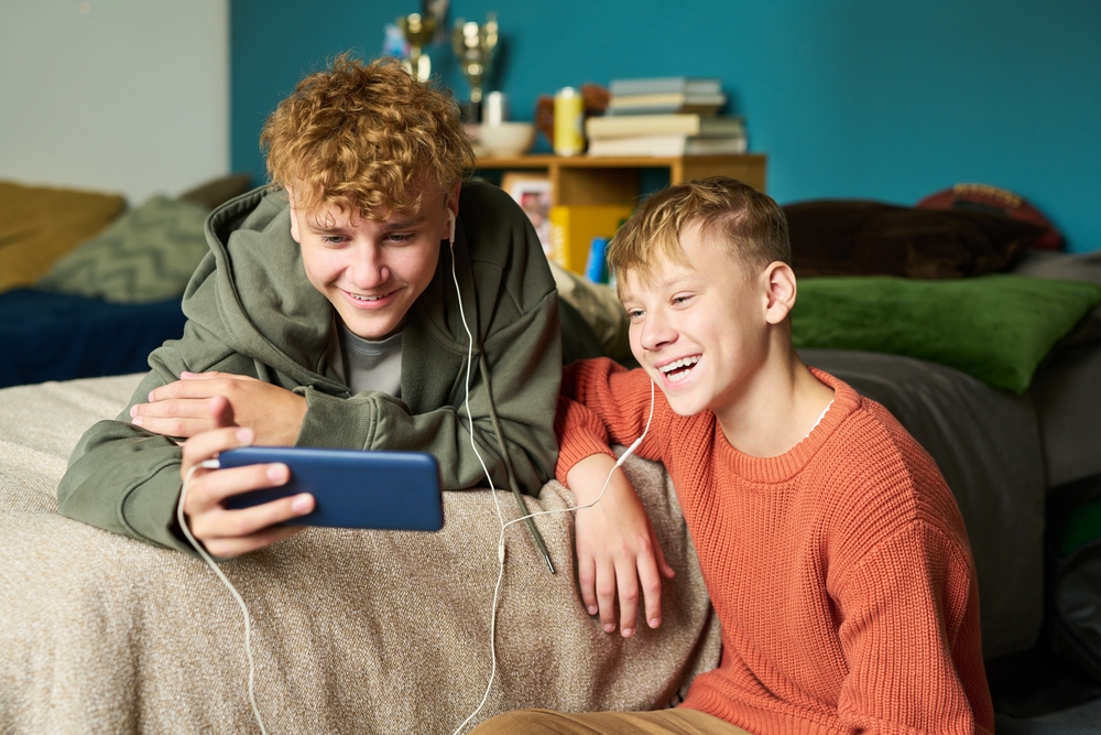 Two teen boys laughing together while looking at a phone
