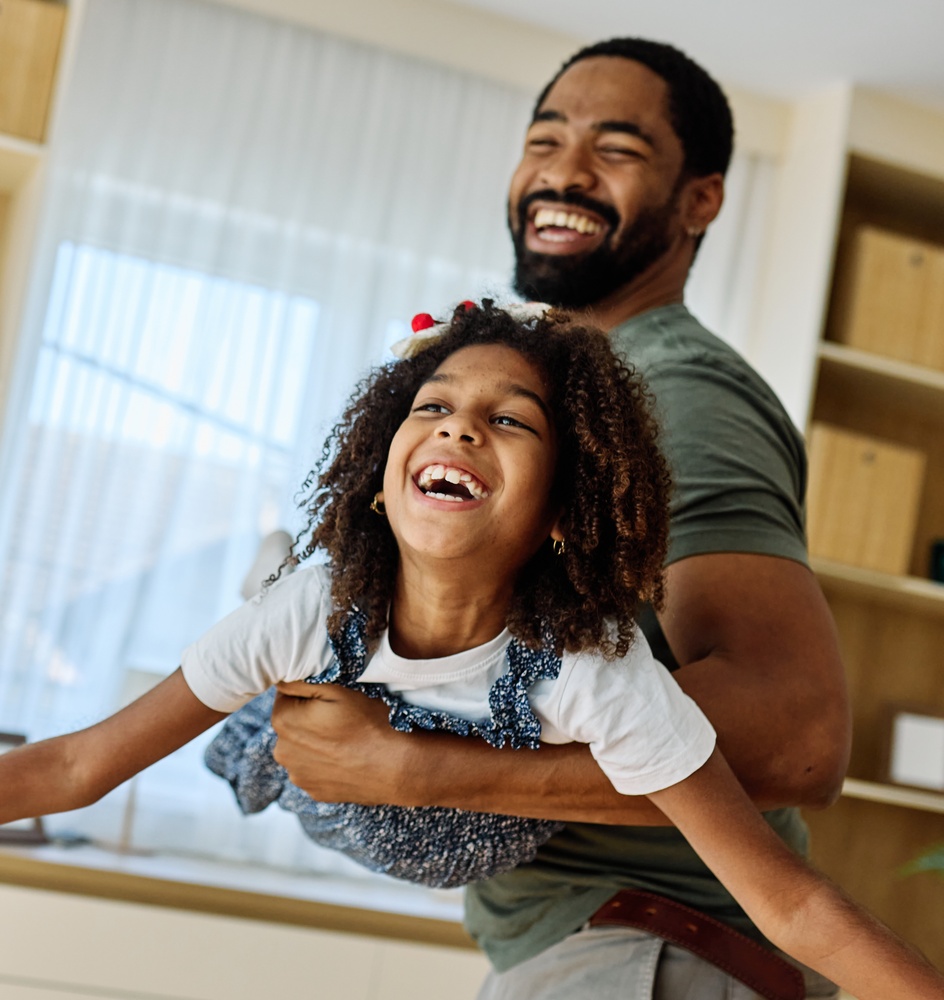 A father laughing while holding his young daughter at home
