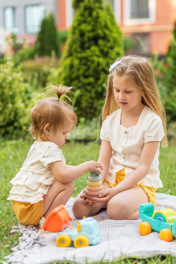 An older sister helping her younger sister stack rings outdoors