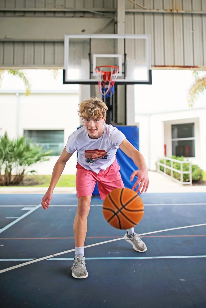 A teenage boy dribbles a basketball on an indoor court