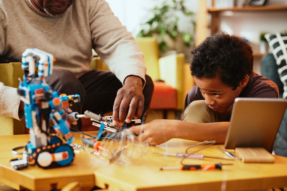 A father and son video call with a provider using a tablet while working on a project together at home
